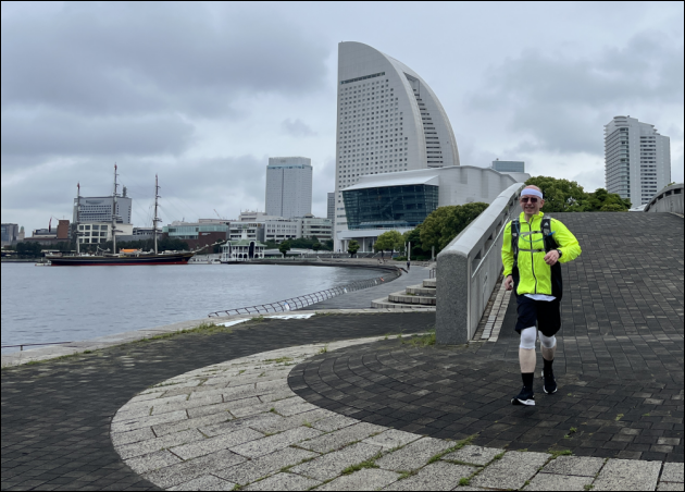 Paul running in Rinko Park in Japan - dayglo jacket and shorts - wearing a TubGrip on each knee - fully rigged saling ship Stad Amsterdam in the background - near the boomerang shaped Intercontinental Hotel